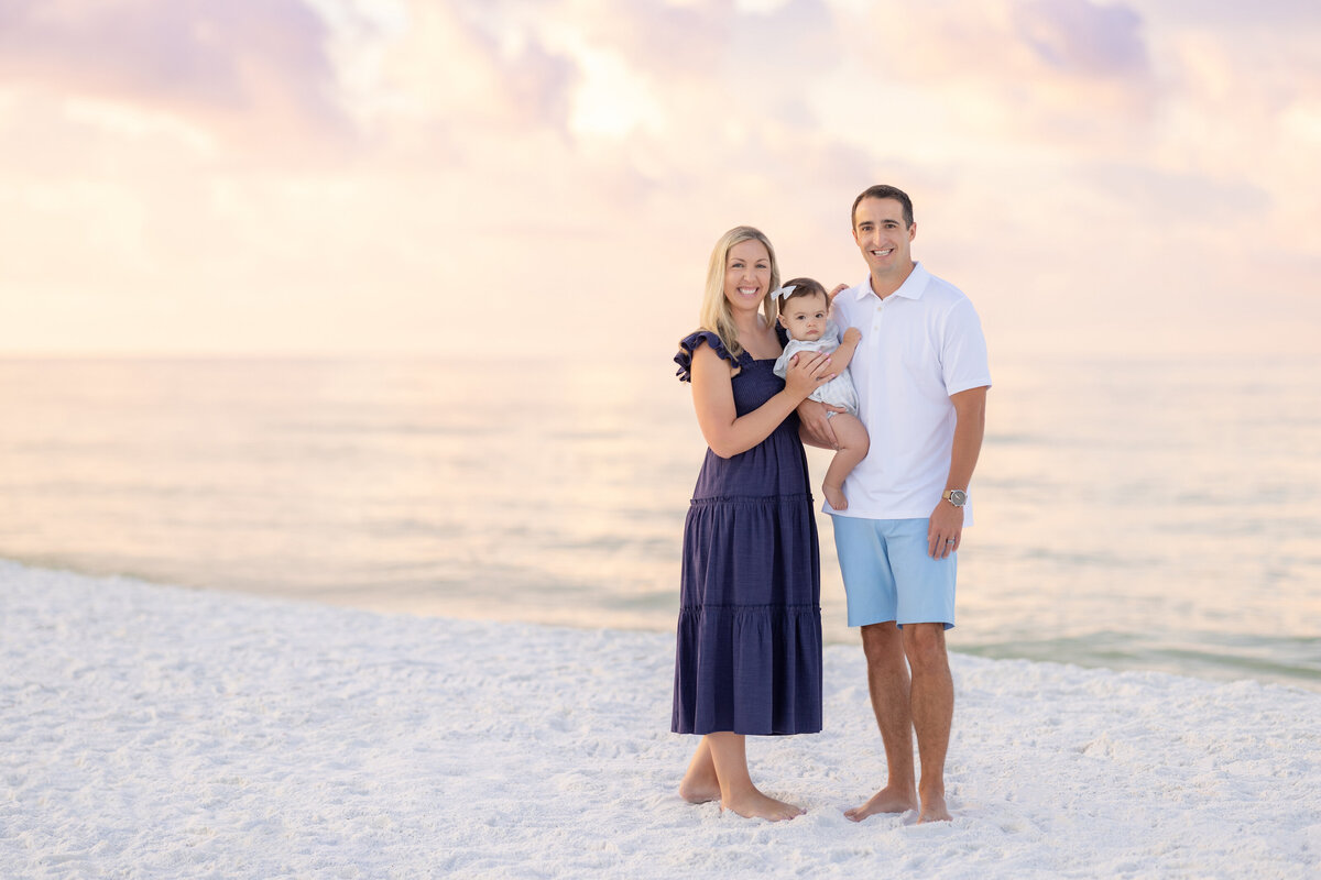 Two parents standing on a beach holding the baby in between them