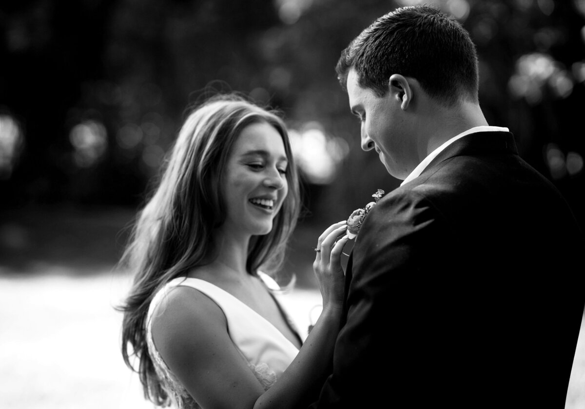 A beautiful black and white of a young couple in their aspen weddings, the bride is touching the grooms flowers pinned to him with a smile.