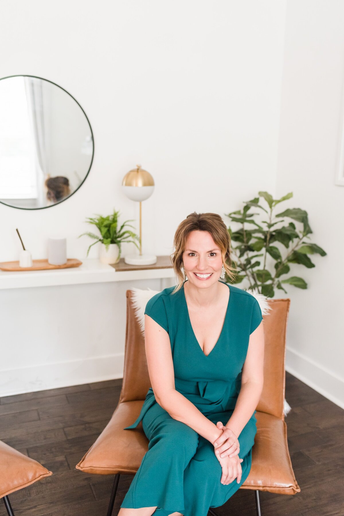 Nashville realtor posed for a casual headshot on a tan leather chair and wearing a green blue jumpsuit