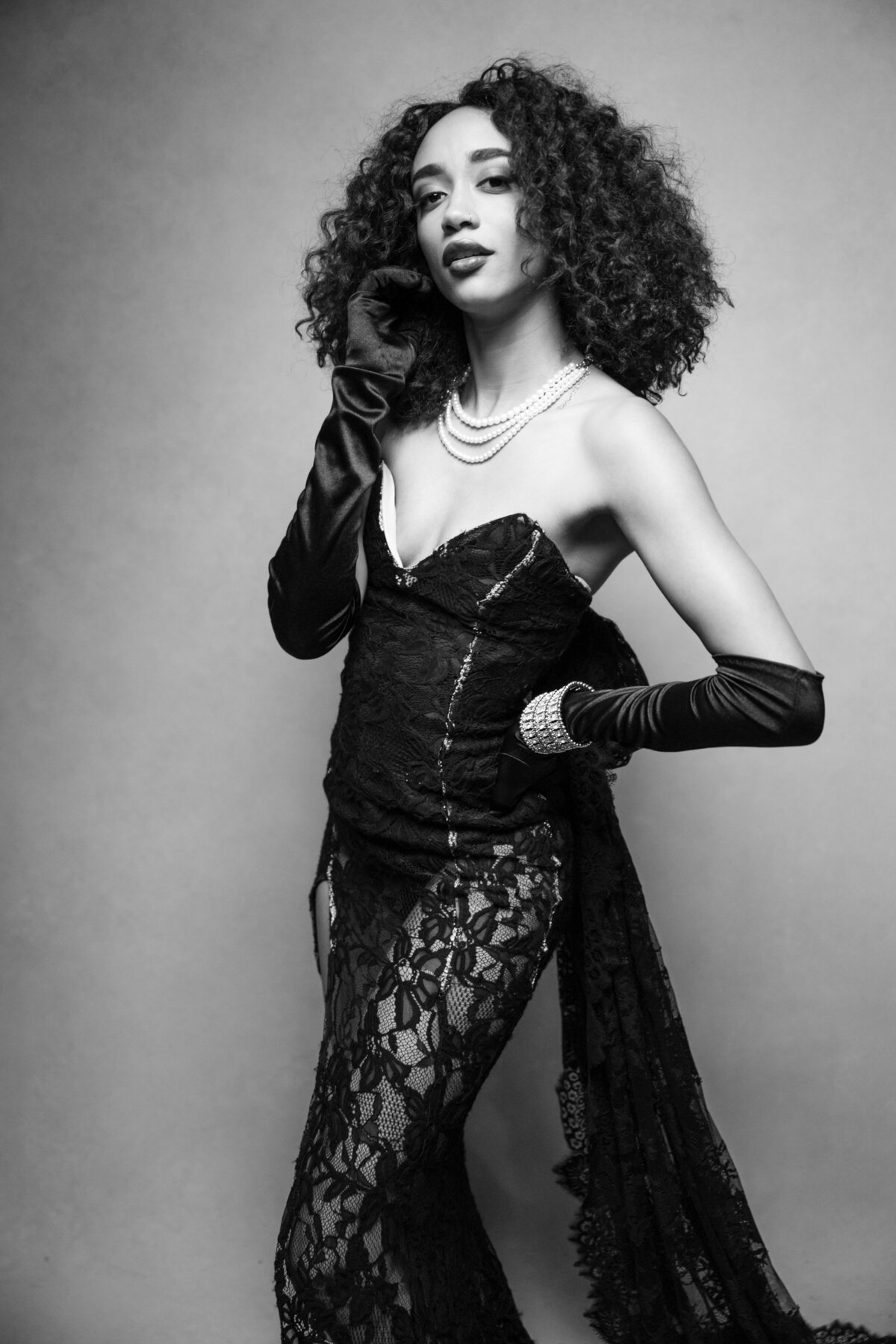 a woman with short curly hair posing with a black strapless lace gown wearing black gloves