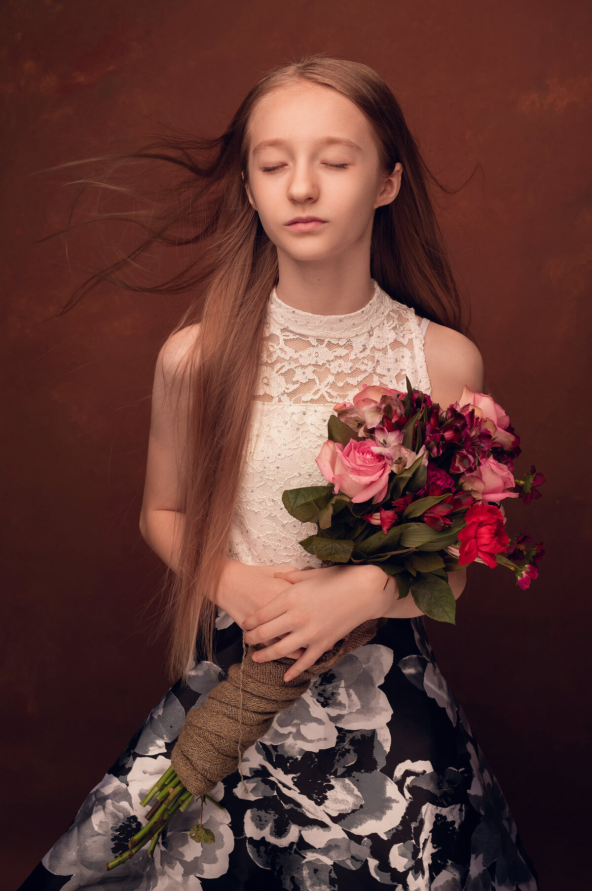 A young girl has her portrait taken in our Waukesha studio while holding a bouquet of roses with her eyes closed and her hair blowing.