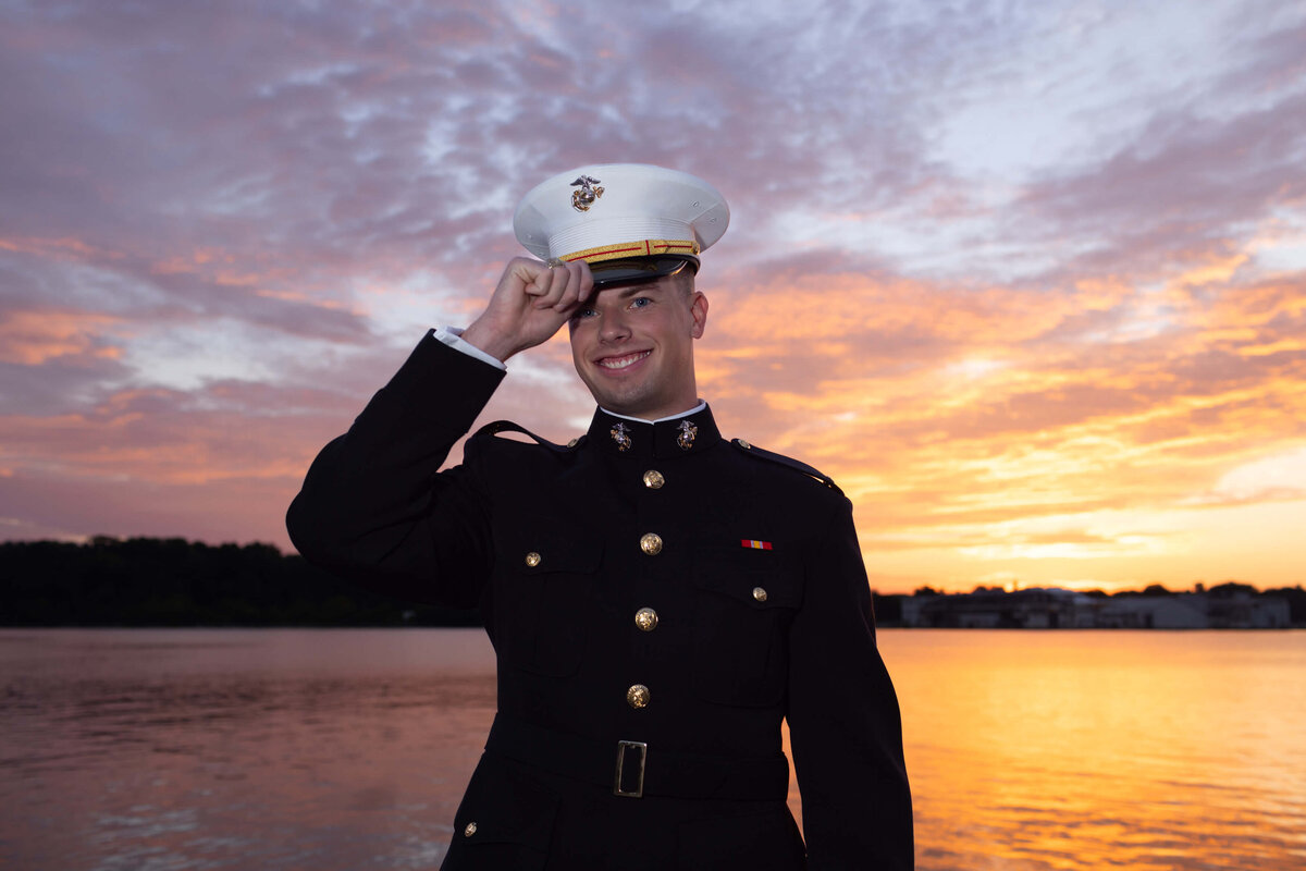 Marine Corps officer and senior at the Naval Academy tips his cover and smiles in front of the Chesapeake Bay during a sunrise photo session with Kelly Eskelsen.