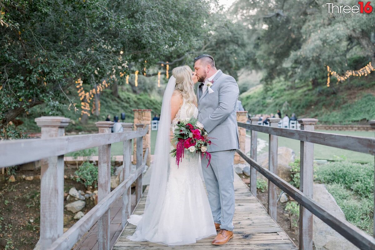 Bride and Groom share a tender kiss while standing on a bridge overlooking the pond