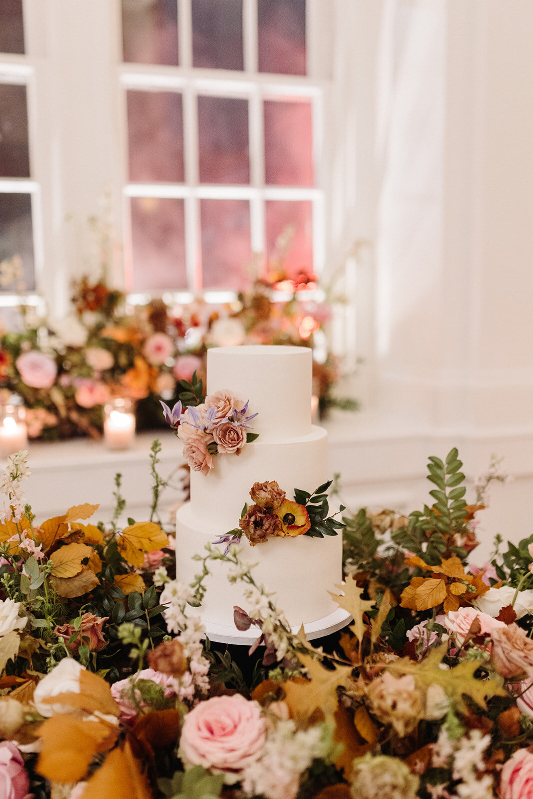 Lush floral meadows surround the cake at this Parisian inspired fall wedding with hues of dusty rose, terra cotta, mauve, copper, and lavender composed of roses, ranunculus, copper beech, clematis, and fall foliage. Design by Rosemary and Finch in Nashville, TN.