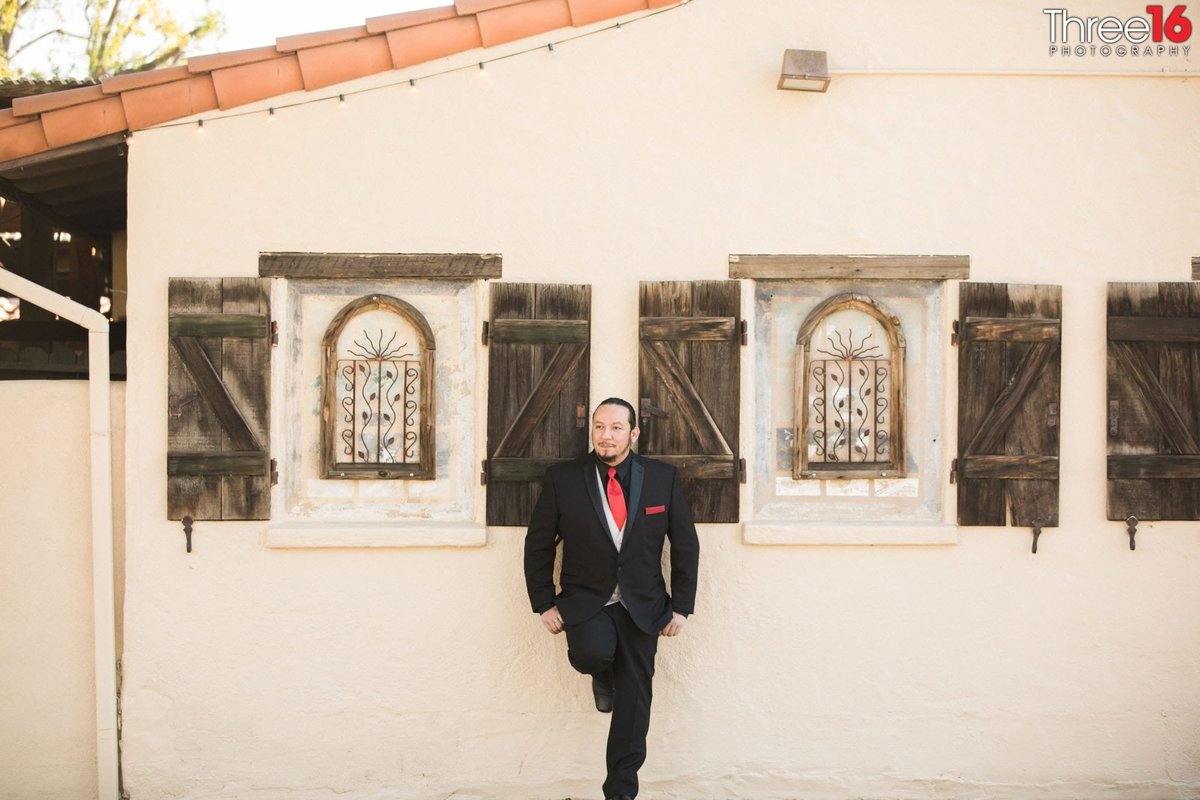 Groom poses with foot on side of The Hacienda building before the wedding