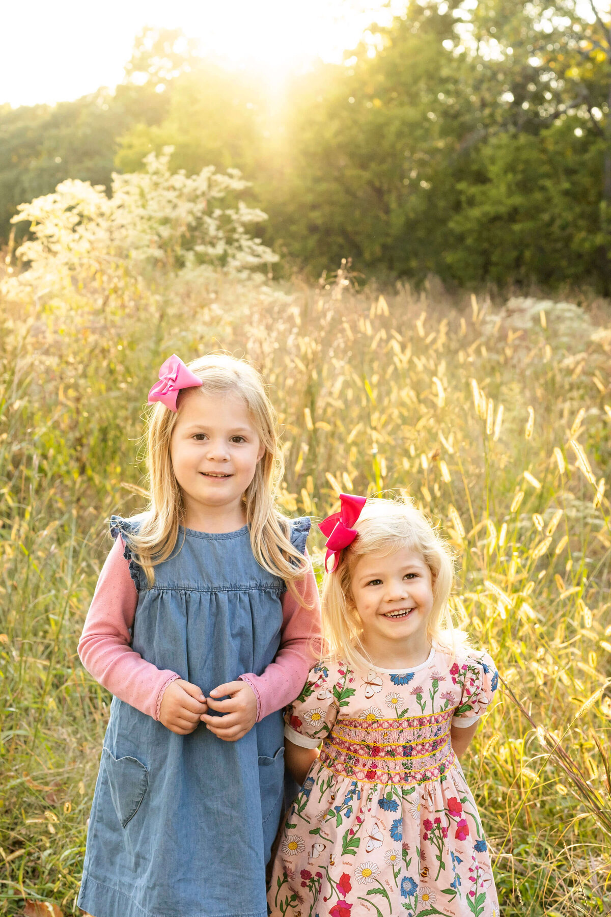 2 young sisters smiling at the camera in a field of tall grass during sunset