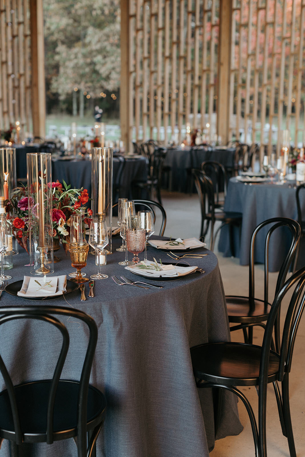 Hudson valley wedding venue with modern reception decor, gray round tables, black chairs, elegant amber accents with red and pink flowers