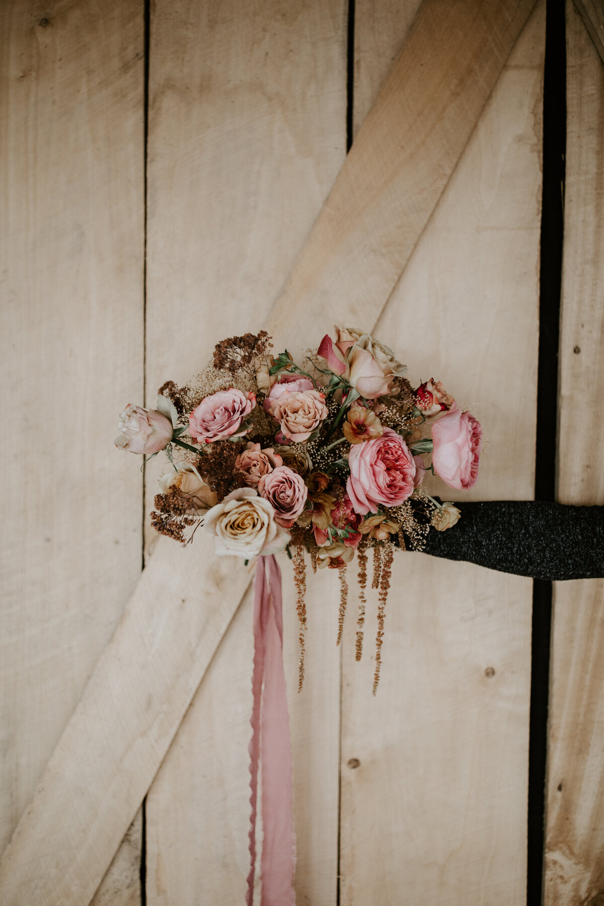 Bouquet of pink and ivory flowers with pink ribbon atop ash-colored wood.