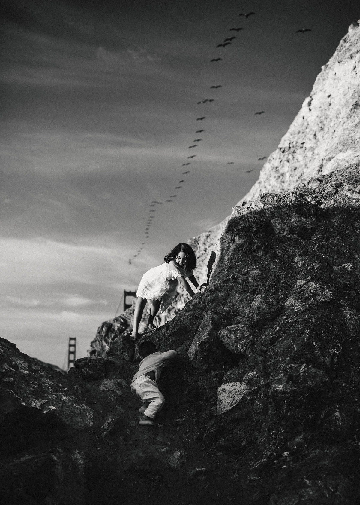Kids climbing rocks at beach with birds flying overhead