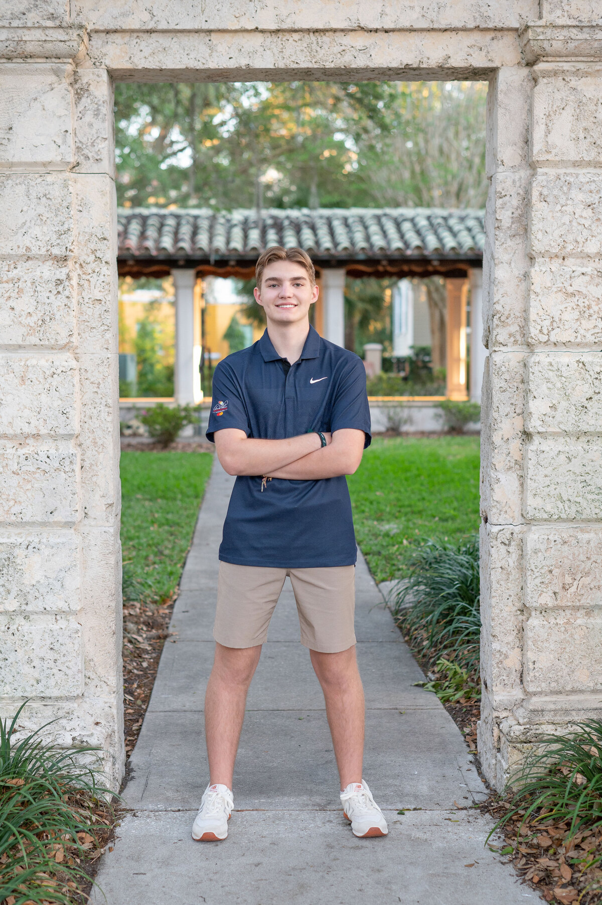 High school senior boy posing with arms crossed between archway by Orlando Senior Photographer Khim Higgins.
