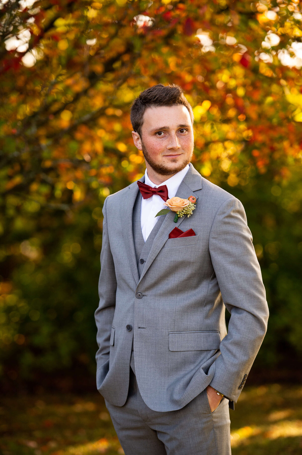 A handsome fall portrait of a groom in a grey suit taken outside in the fall at Strathmere wedding venue.  Captured by Ottawa wedding photographer JEMMAN Photography