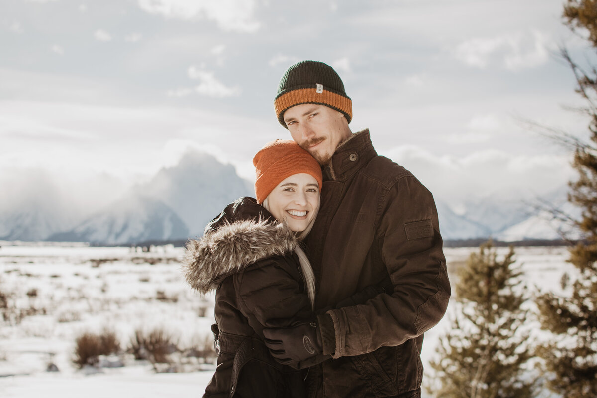 jackson hole photographers captures couple holding each other in winter  in front of the Grand Tetons for their winter engagement session