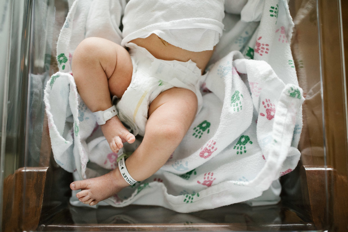 Newborn baby in a white diaper wearing hospital bands around ankles by Laurie Baker