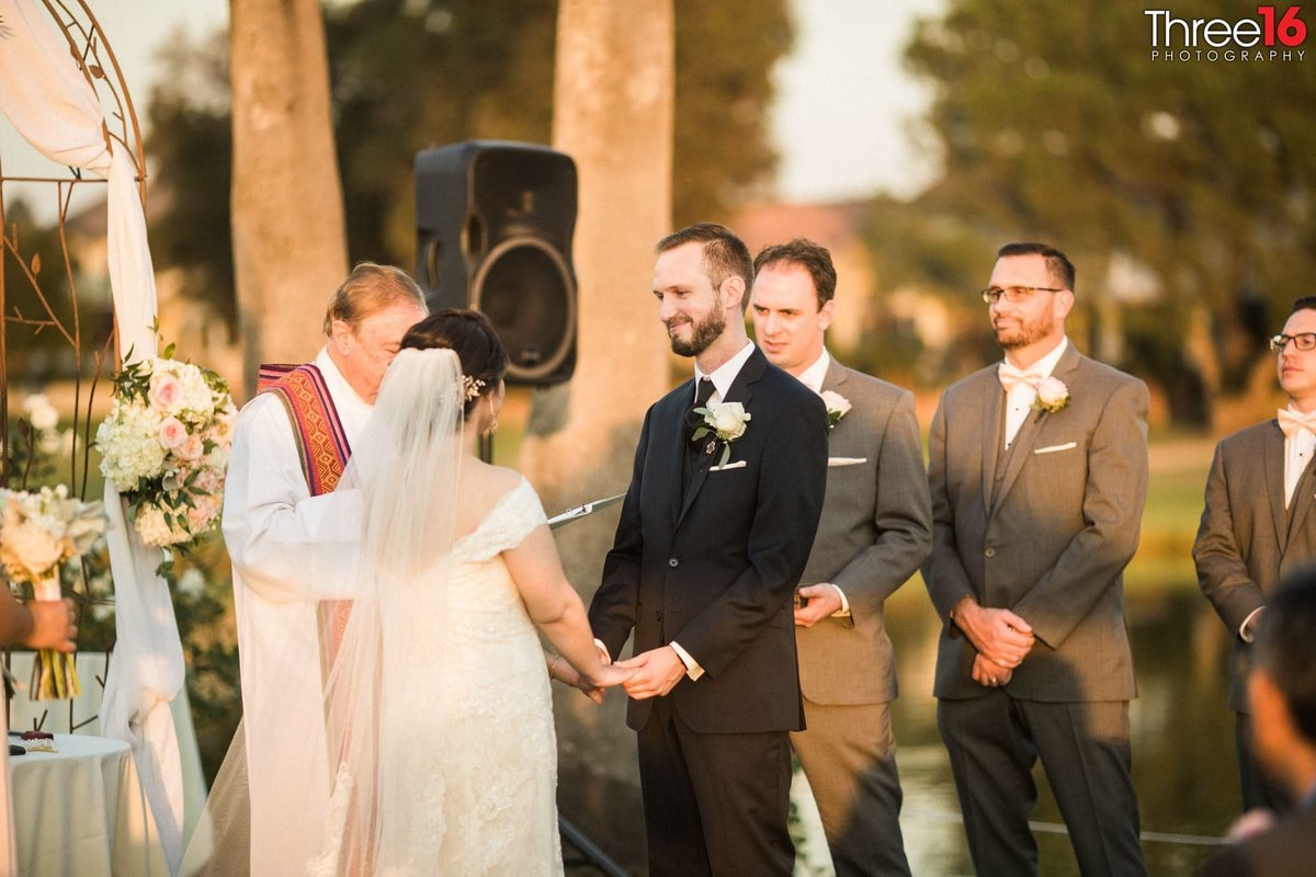 Groom smiles at his Bride as they hold hands at the altar