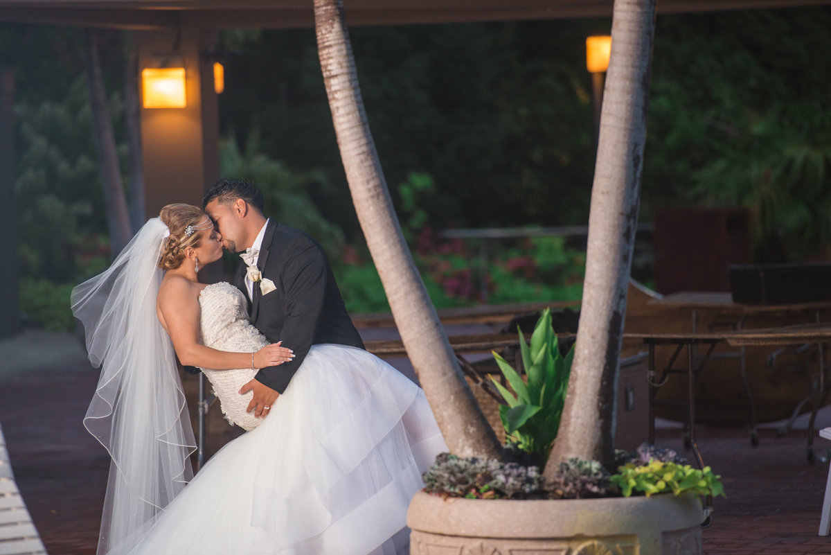 Bride and groom kissing by the palm trees at Crest Hollow Country Club