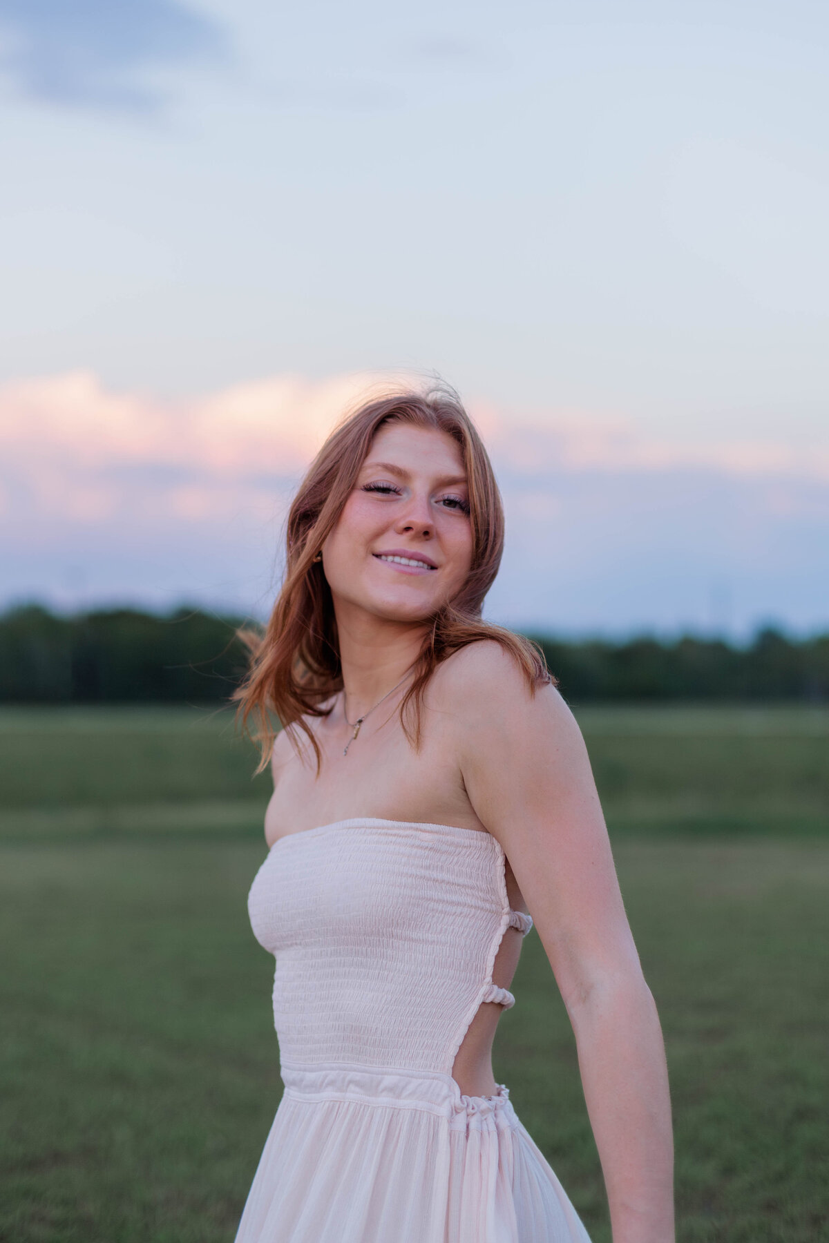 Headshot of a high school senior girl at sunset with fluffy pink clouds behind her