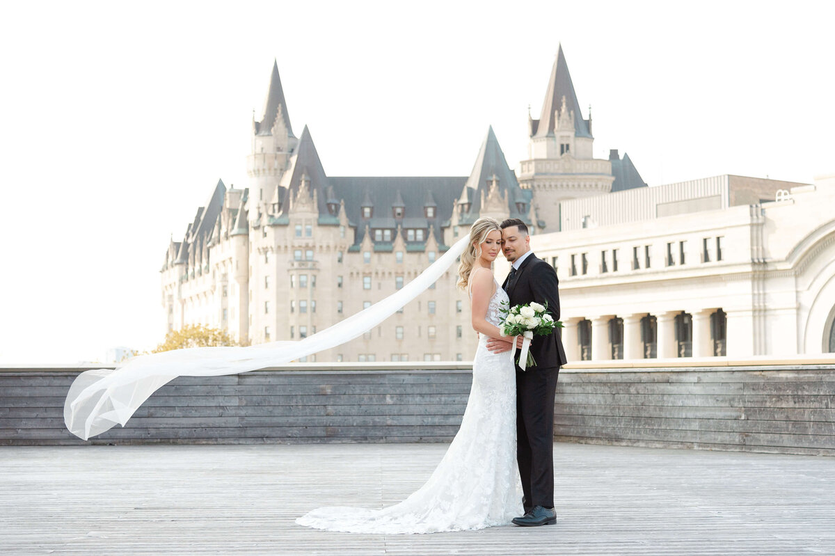 a photo of a groom and bride with her veil blowing in the wind taken outside the NAC by Ottawa wedding photographer JEMMAN Photography