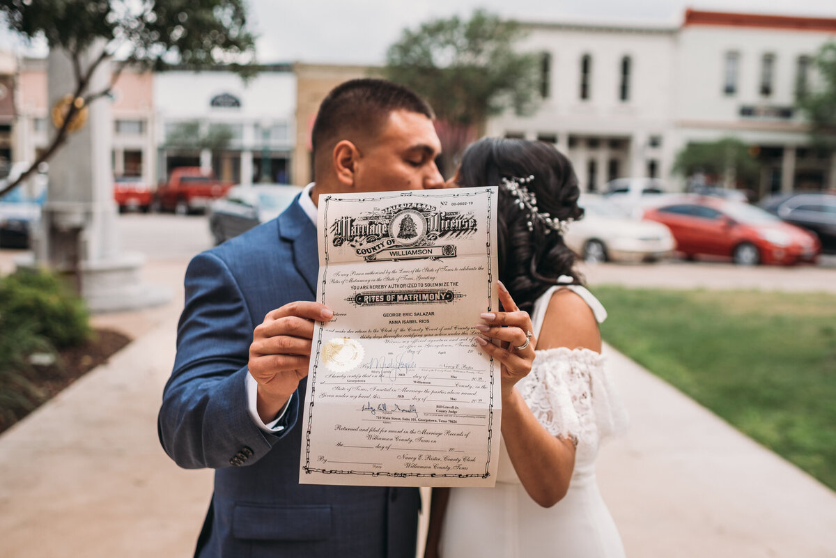 Couples Photography, bride and groom hold up marriage certificate outside and kiss