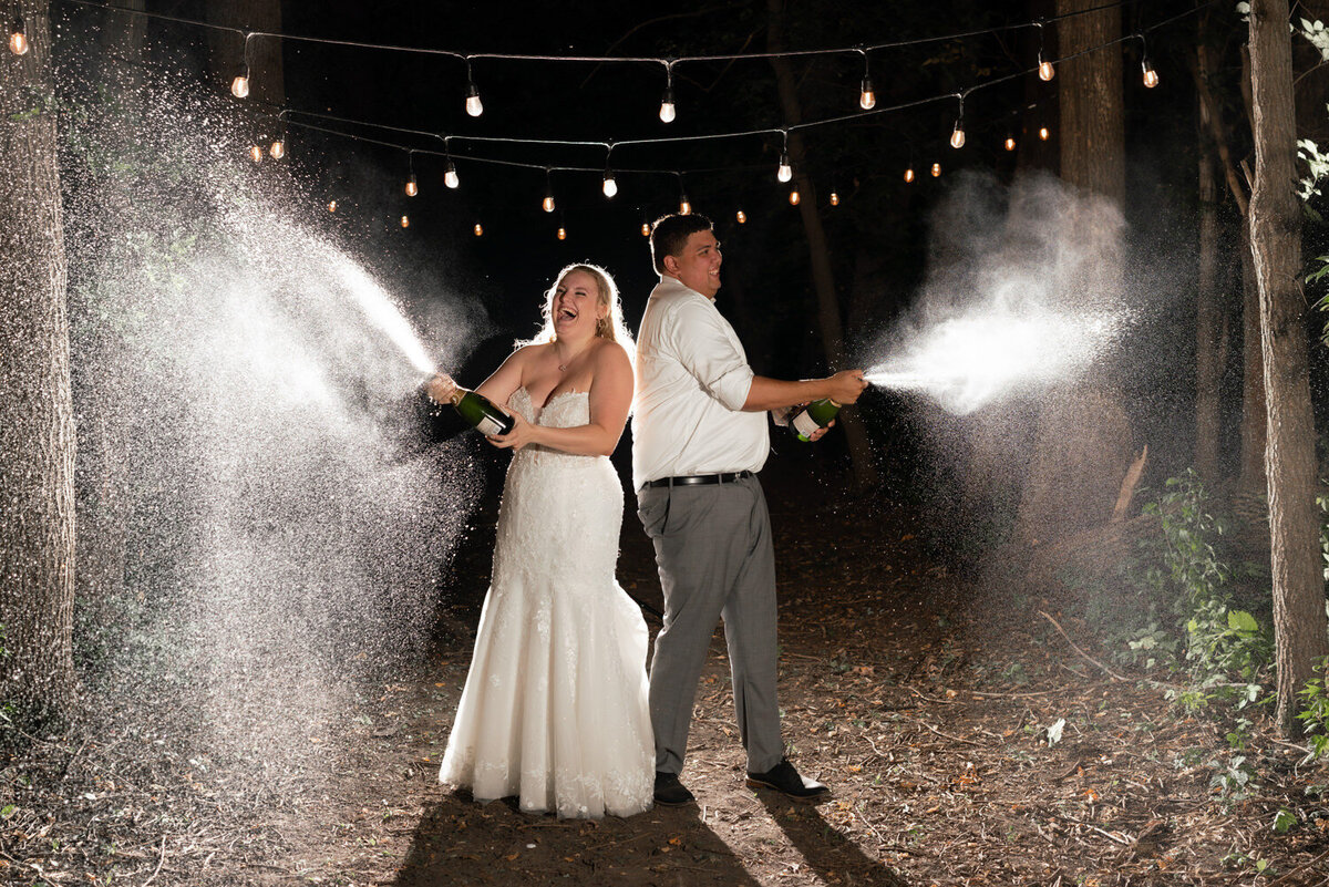 Bride and groom spray champagne and laugh at night.