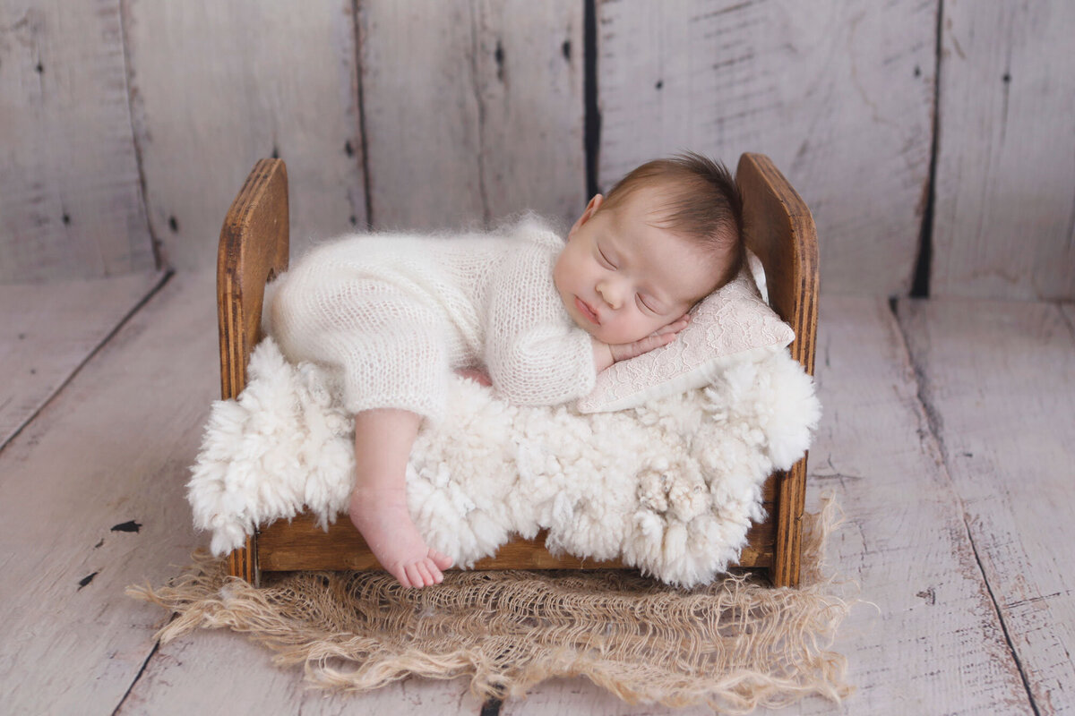 Oakville-newborn-photographer-busy-with-a-newborn-baby-girl-poses-in-a-wooden-bed
