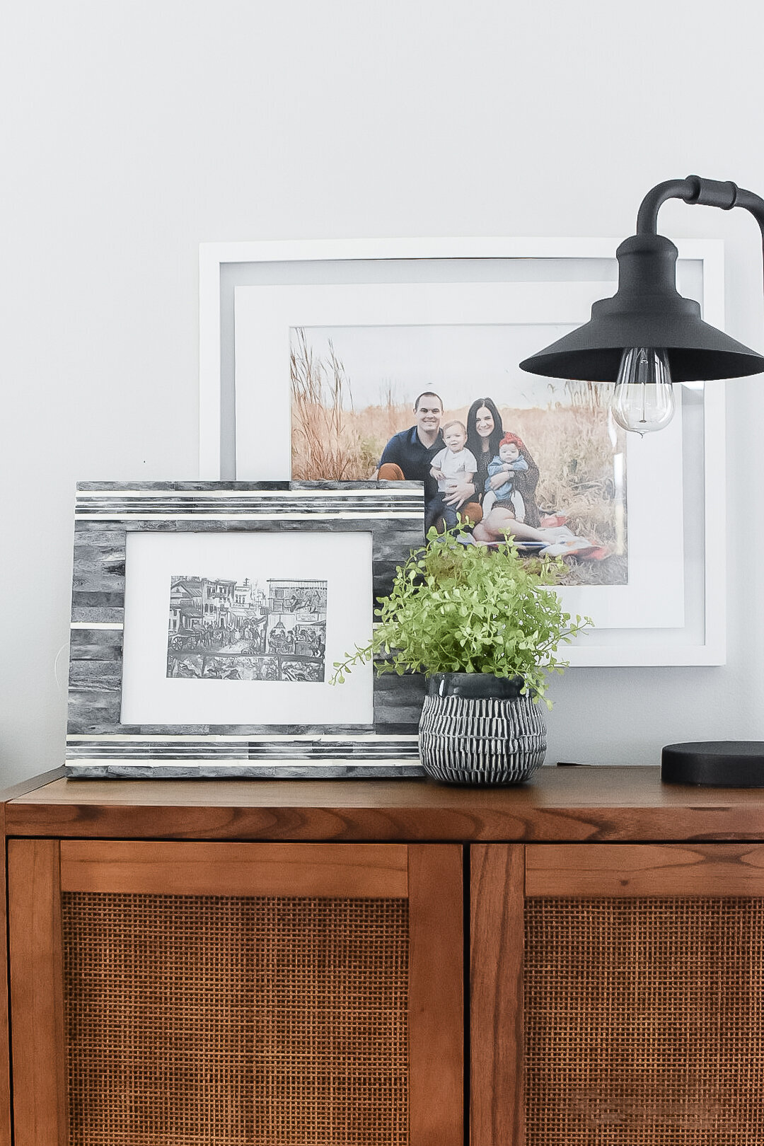 Multiple photos sitting on a wooden console with a black lamp