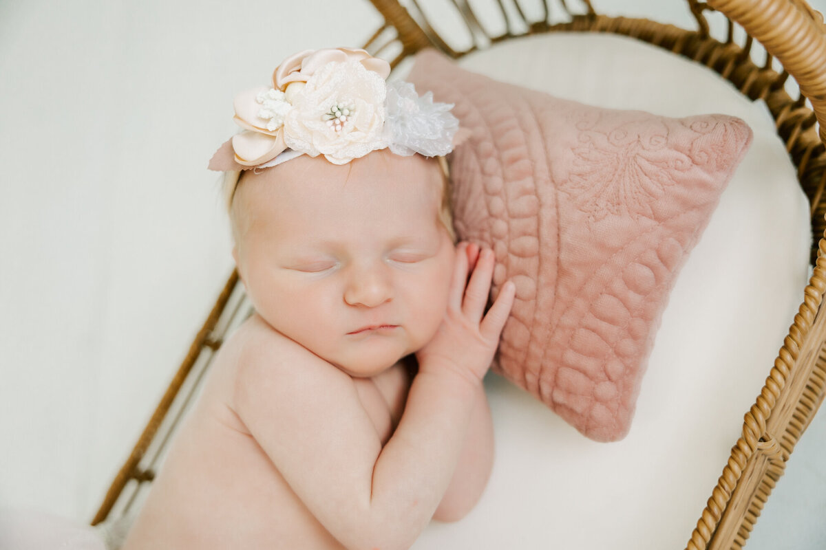 baby girl sleeps on blush colored pillow with floral headband.