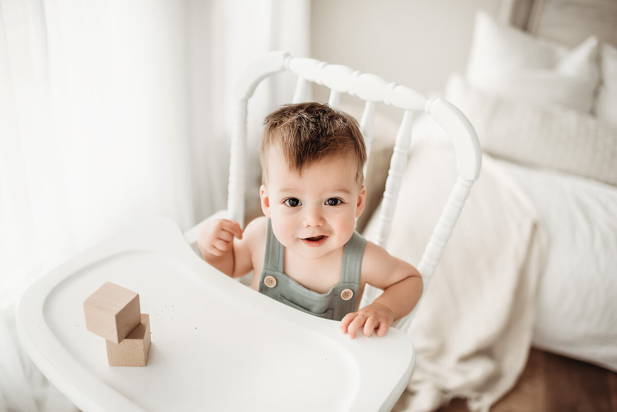 one year old milestone boy sitting in white high chair looking at denver photographer
