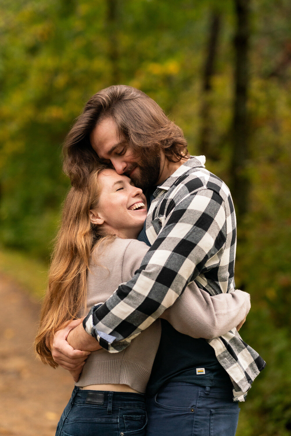 Man and woman in flannel and jeans with long hair hug in the forest.