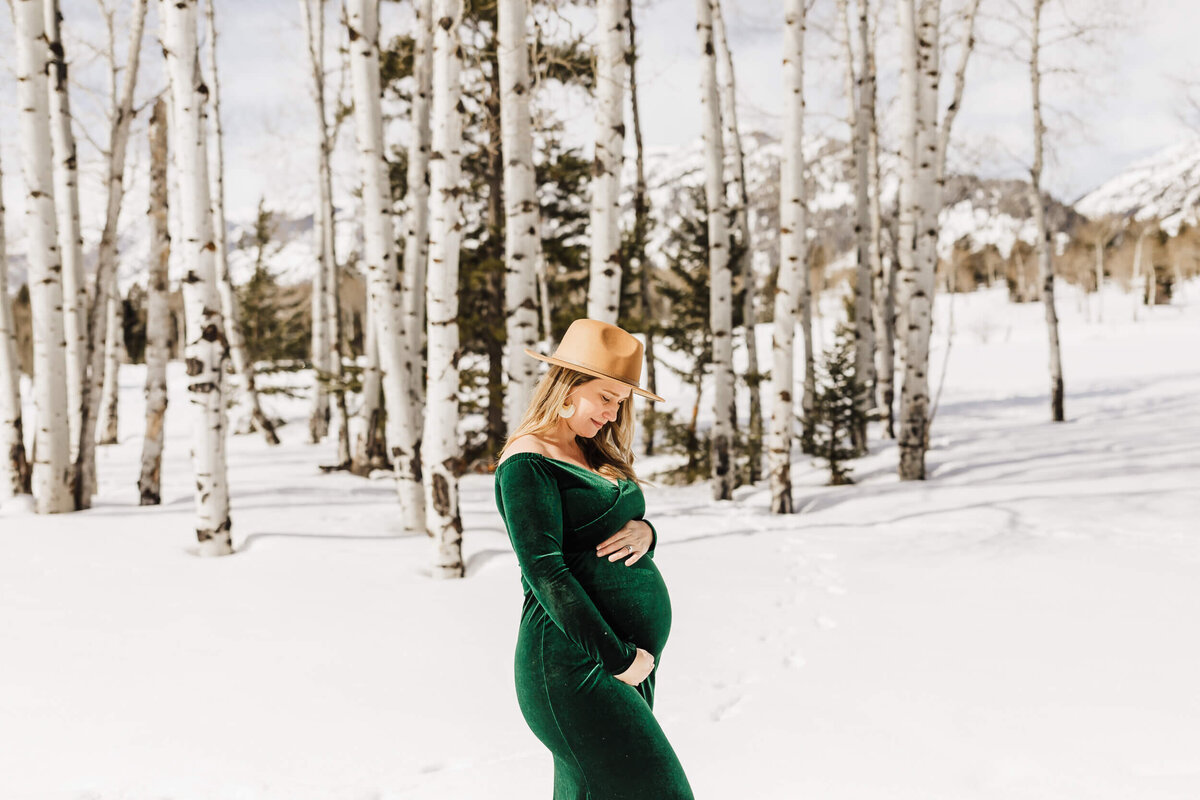 Pregnant mother holding belly on a background of snow and birch trees.