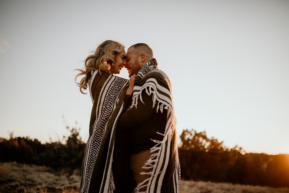 engaged couple wrapped up in a blanket together in the desert