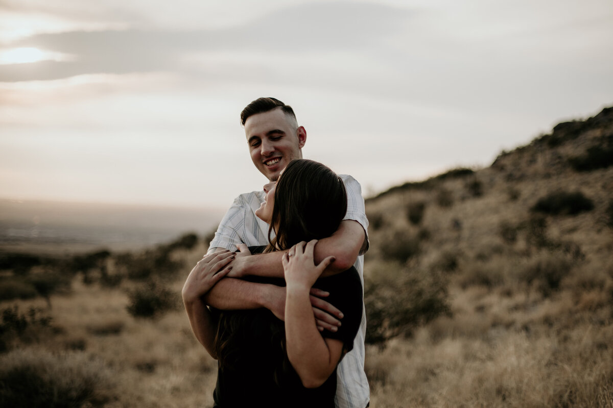 man hugging fiancé from behind in the desert