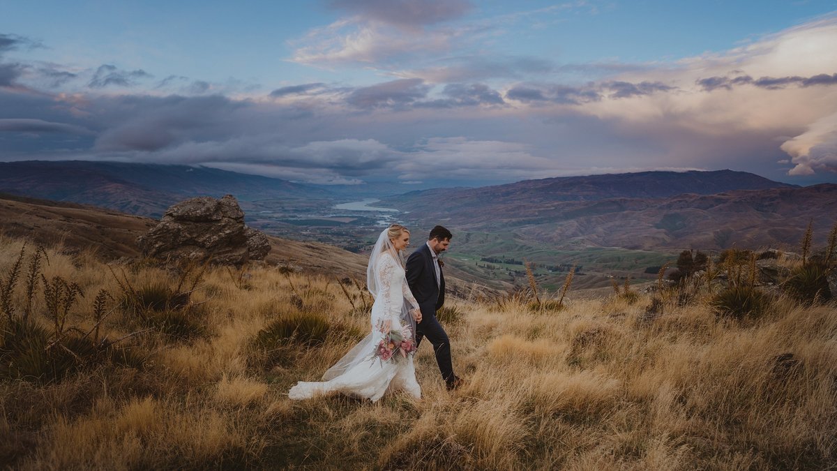 bride and groom walking through golden grass in the hills of bannockburn
