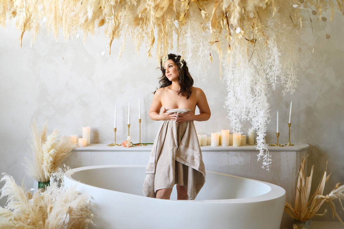 Brown-haired woman holding towel standing in a tub for her Mississauga boudoir photography session.