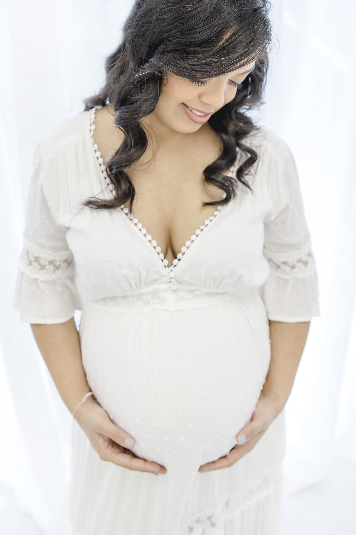 Pregnant woman in white dress looking down at belly