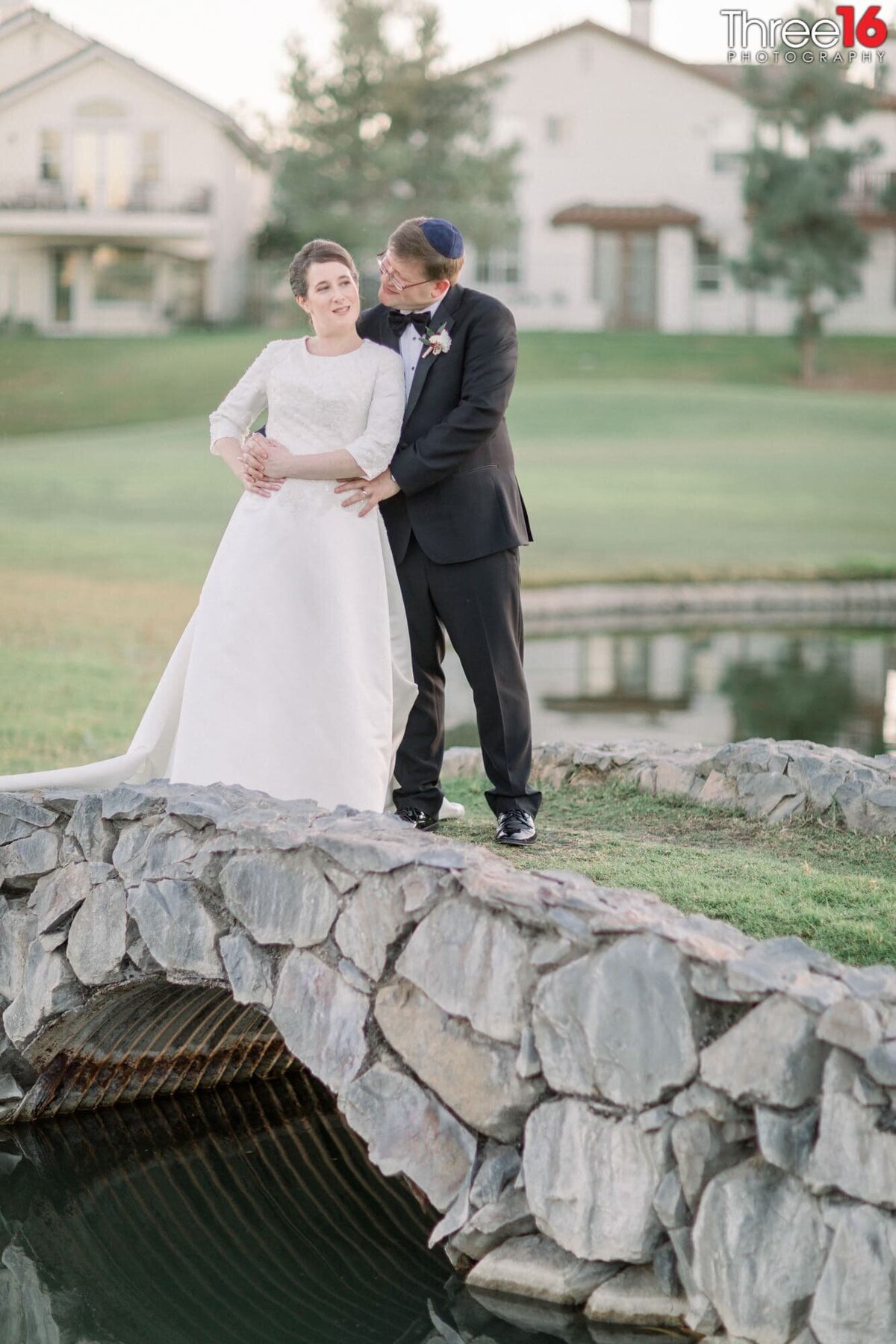 Married couple pose together on a grassy bridge going over a creek on the golf course