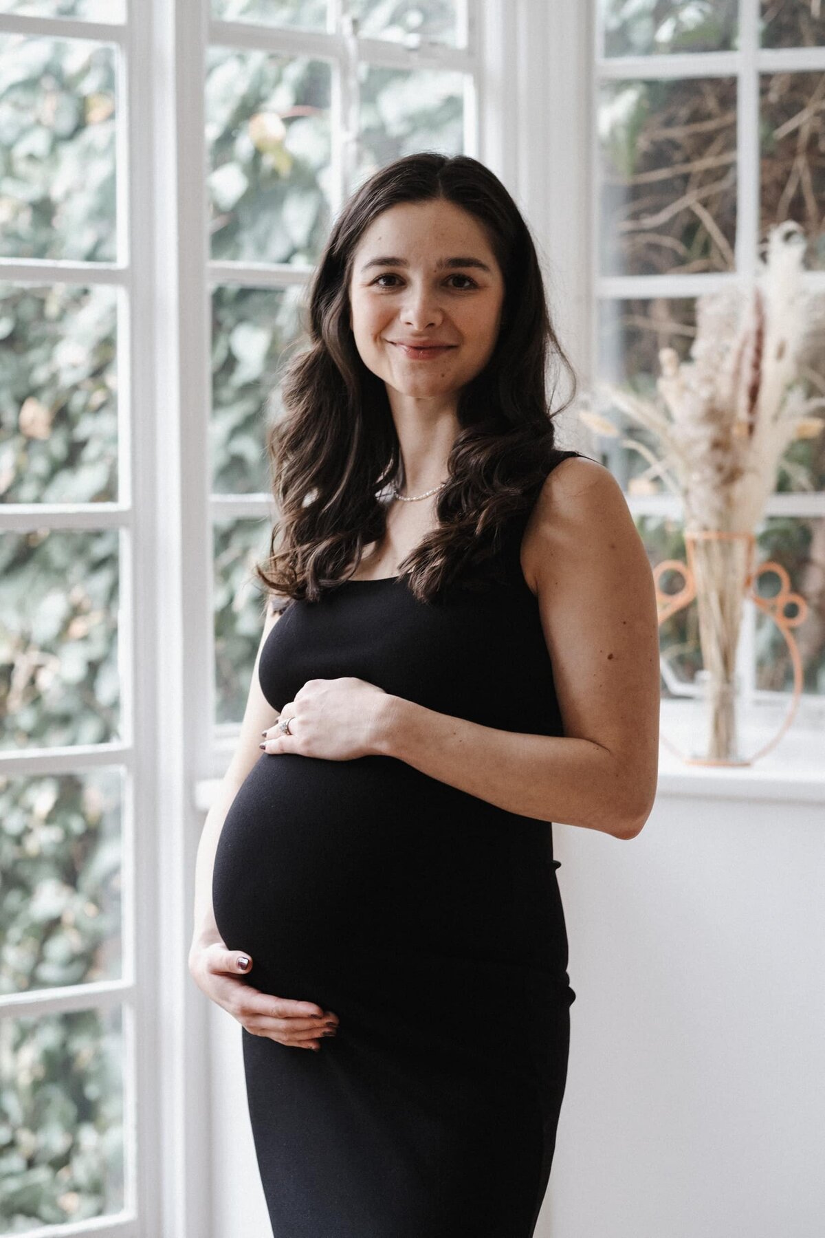 Long haired pregnant woman stands in living room and smiles