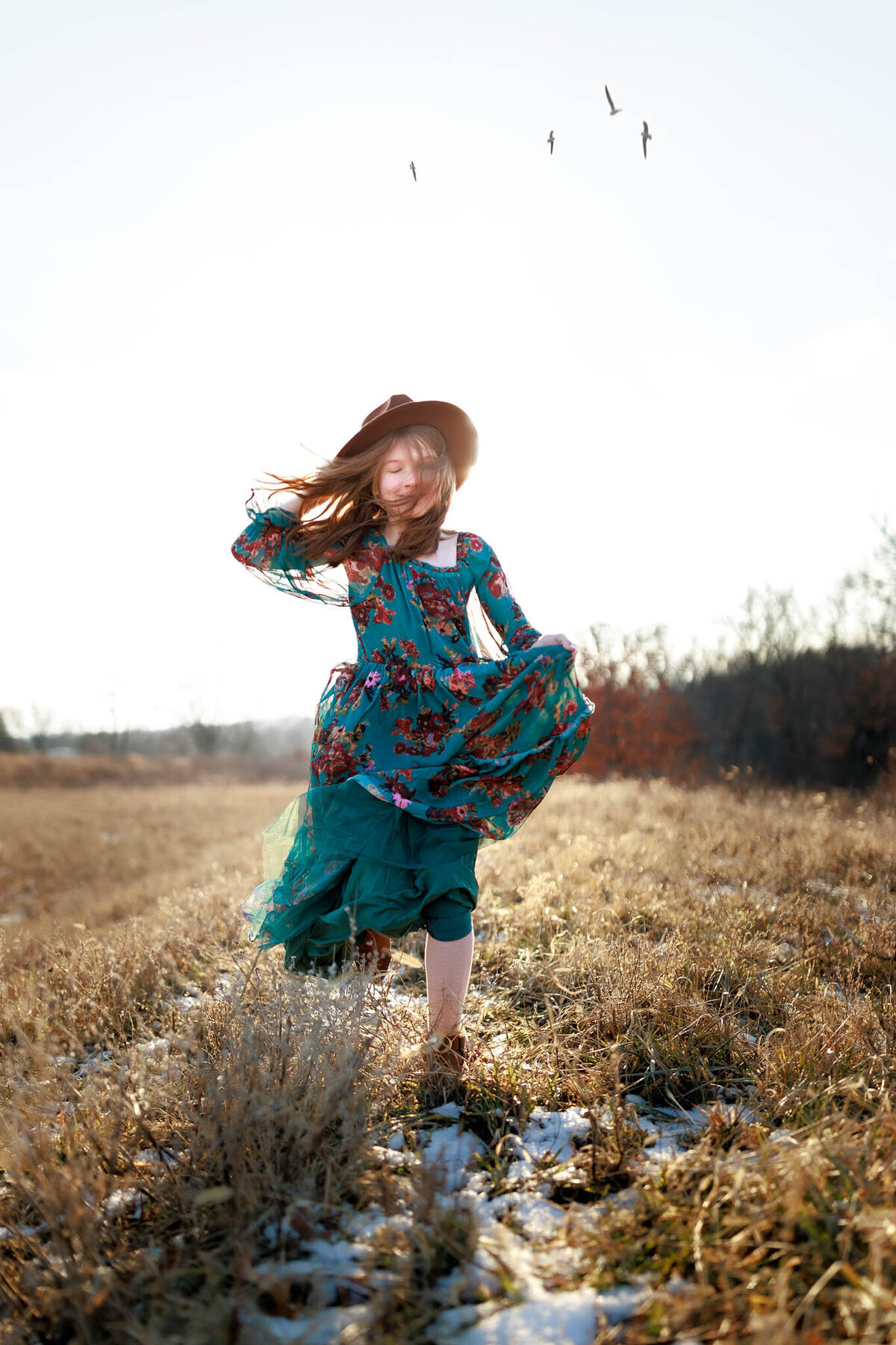 girl in winter running through field with floral dress and fedora
