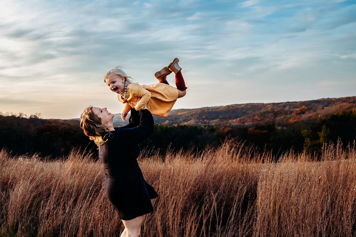 Mama lifting daughter in air with wheat grass and blue clouds