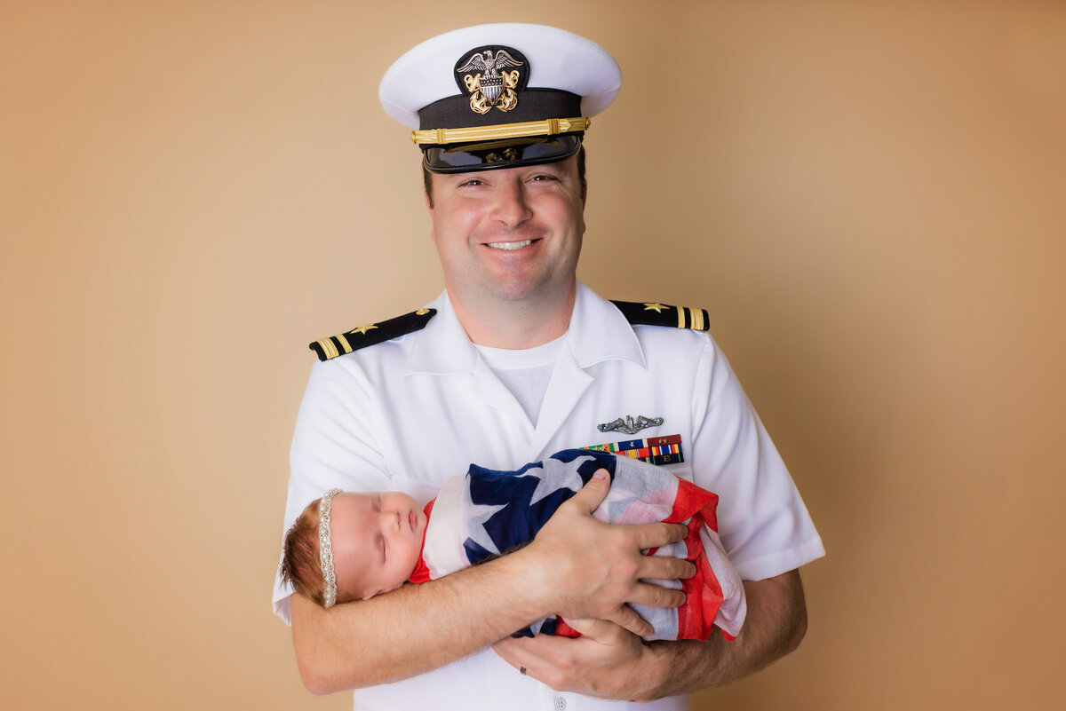 Newborn Photographer, a US Serviceman holds baby girl wrapped in an American flag