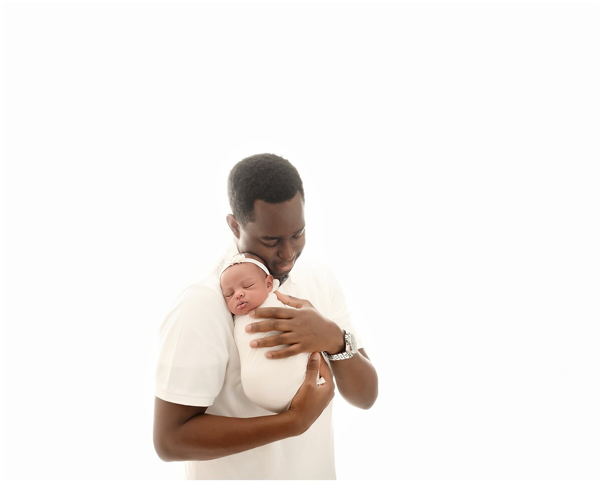 A portrait of a newborn baby girl gently nestled in her fathers arms.