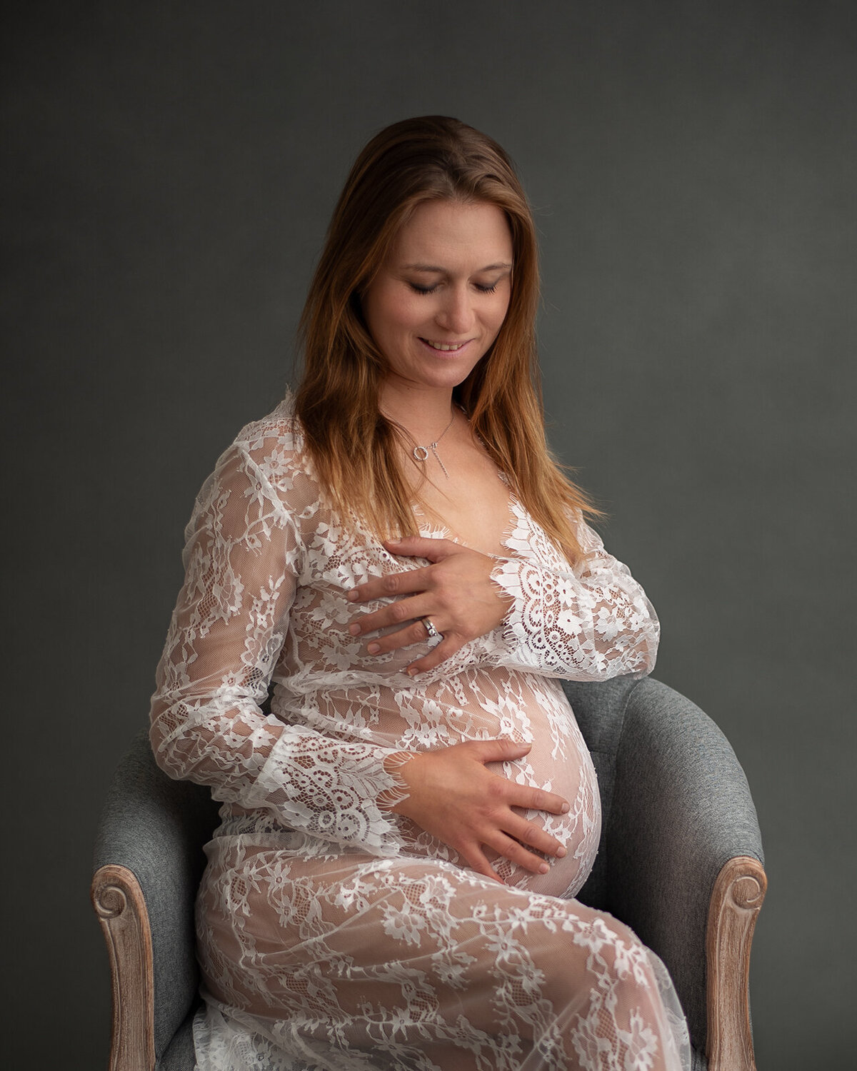 pregnant woman sitting in lace gown looking at belly by st. louis maternity photographer, sutherland photography