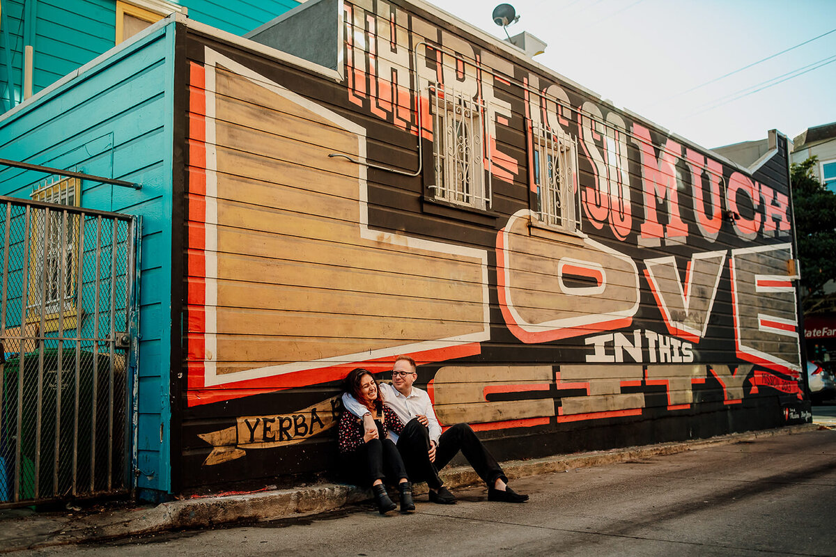 Bay Area engagement couple sitting in front of mural in Mission District of SF.