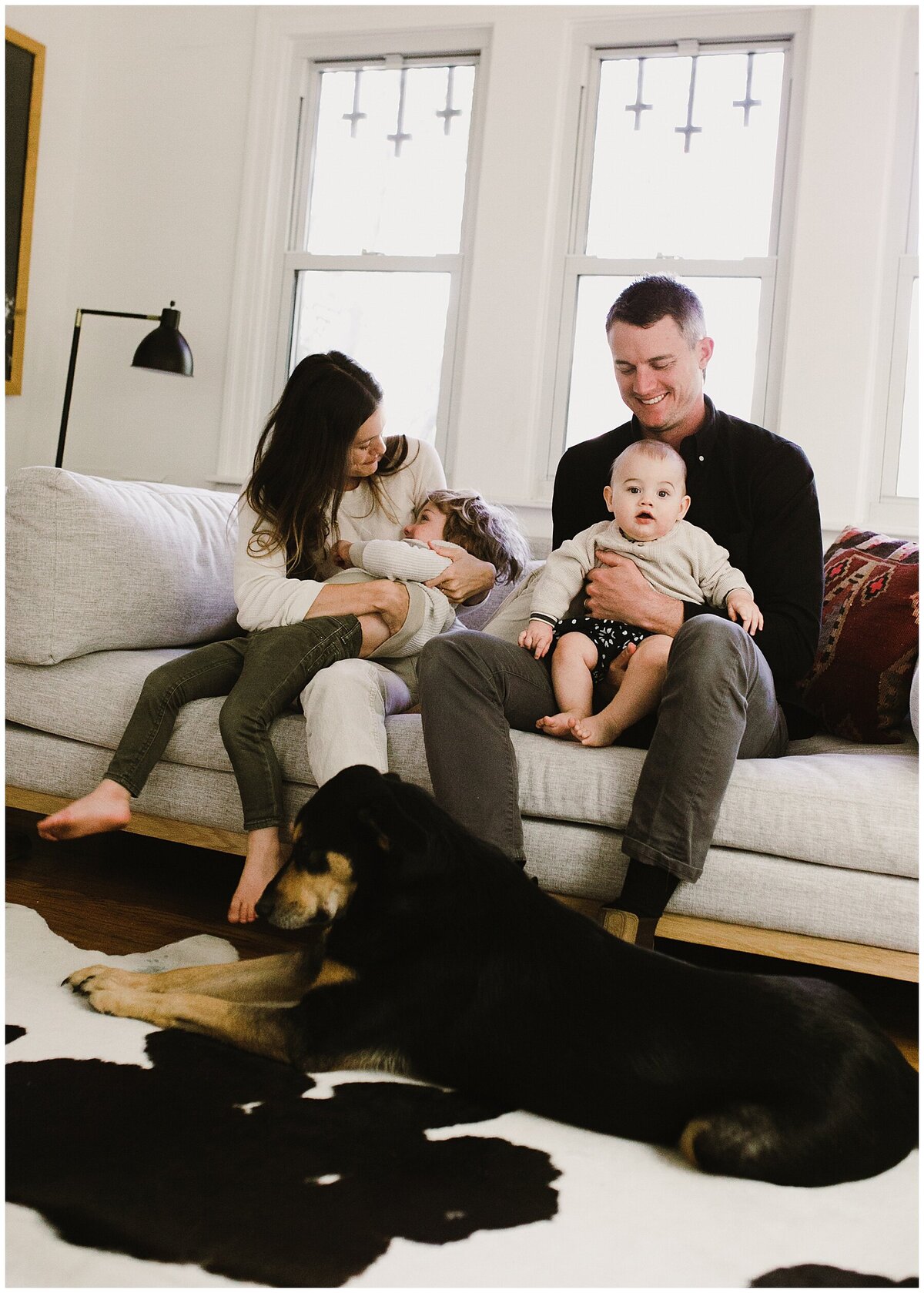 Family with baby and toddler sitting on sofa with dog laying on rug at  sweet at home family session in Austin by Amber Vickery Photography