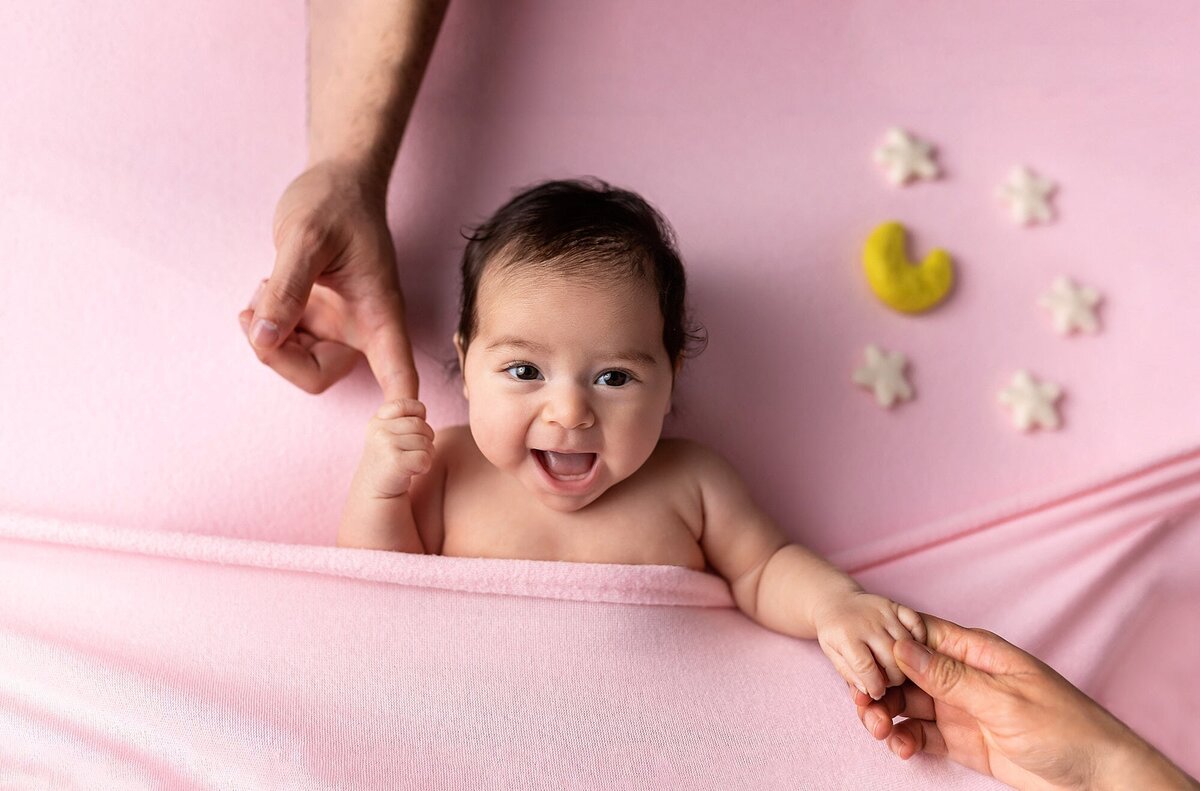 Baby in pink blanket holding parents' hands