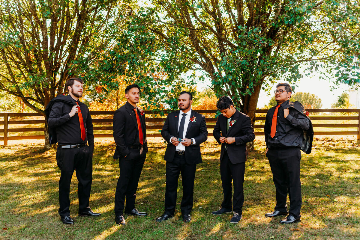 photo of a groom and his groomsmen adjusting their black suits in front of a fence
