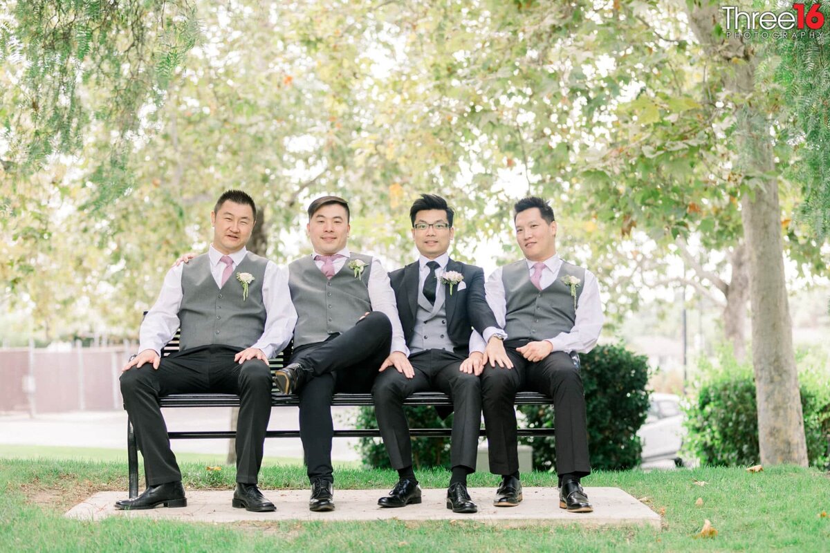 Groom sits on a park bench with his Groomsmen before the wedding ceremony