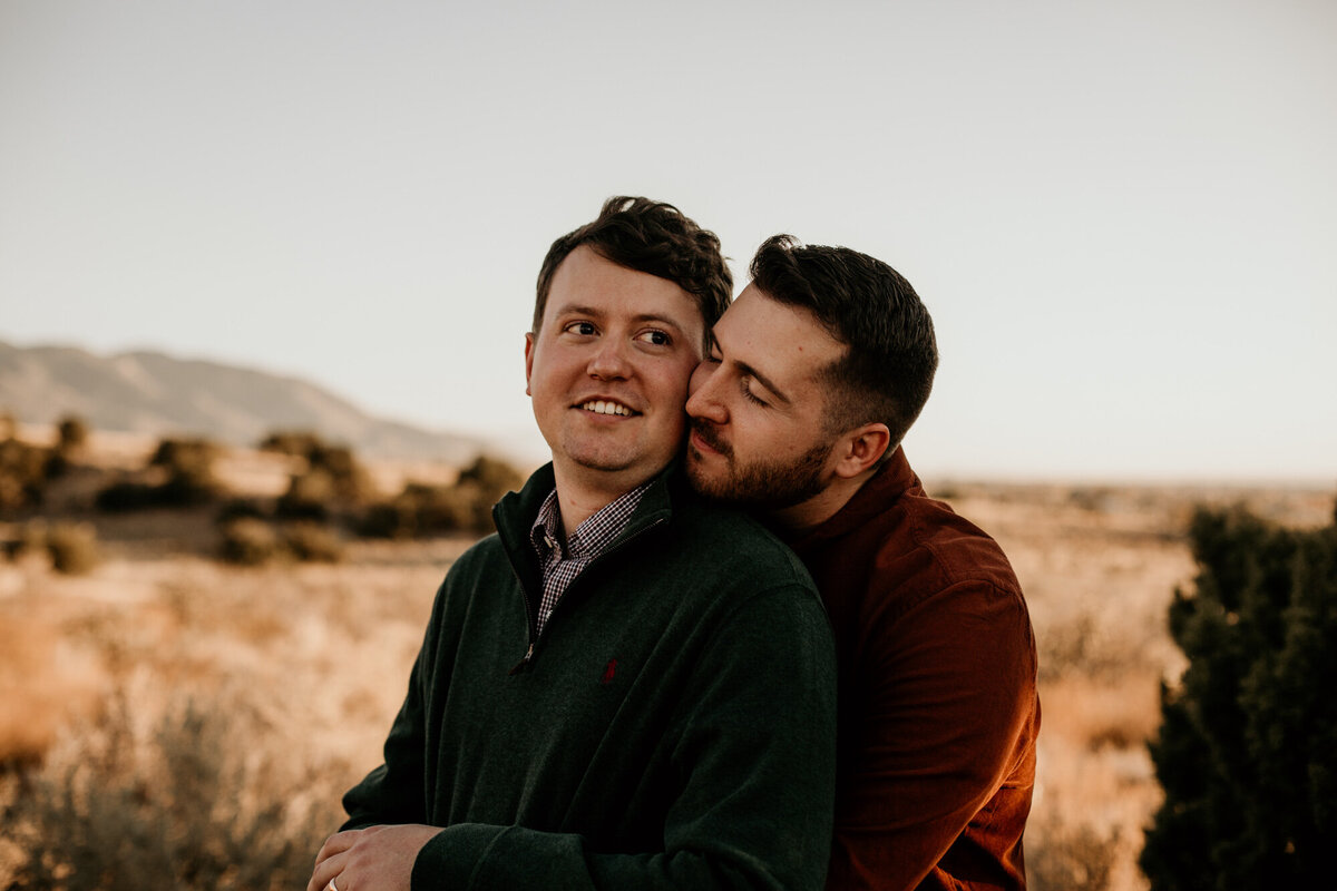 man kissing same sex fiancé on the cheek from behind