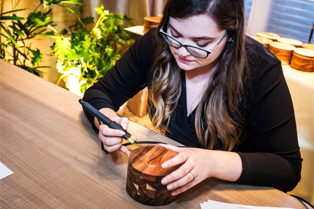 emily pellegrino sitting at a table working on wood burning onto spice jars with calligraphy