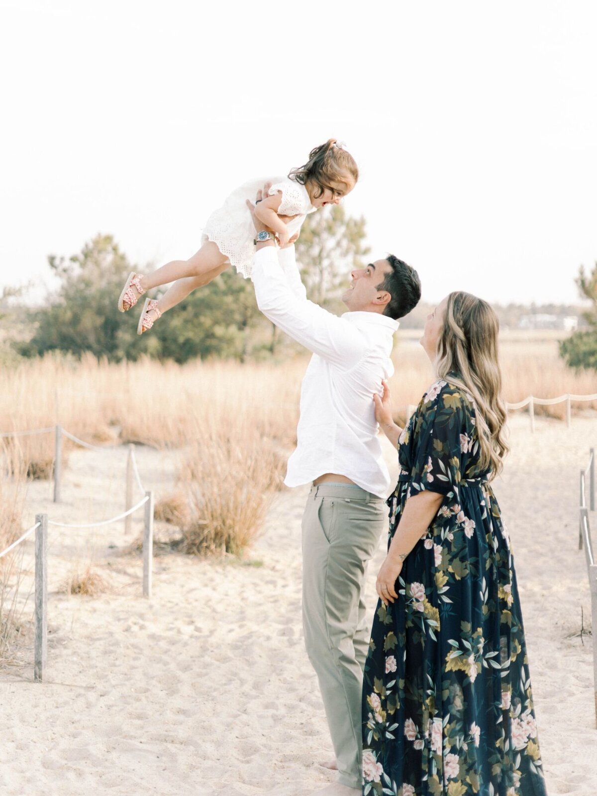 Fathers throws daughter up in air playfully with mother smiling.