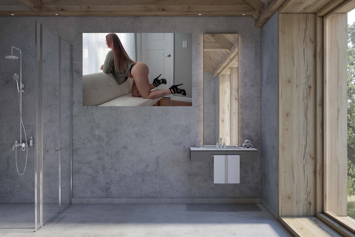 A large canvas that is hung on the wall in the bathroom. It is a pic of a woman wearing a sweater and panty. She is kneeling on a couch and looking out the window.